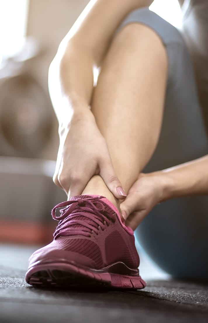 Person grabbing their ankle wearing red running shoes