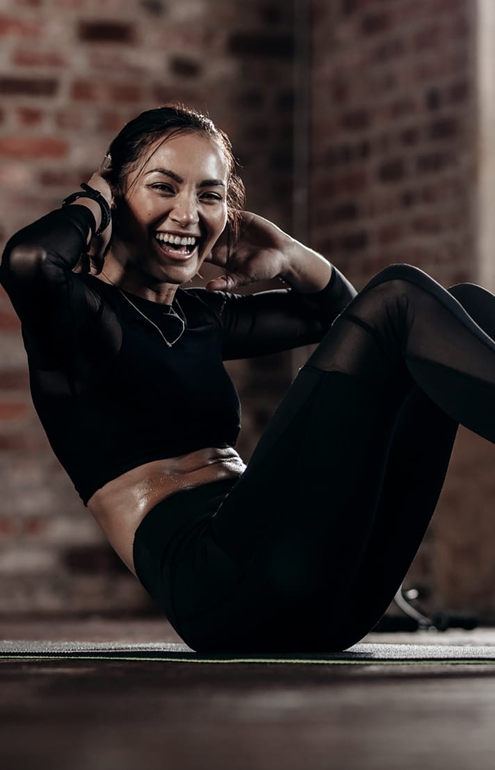 Pretty woman wearing black workout outfit smiling while doing a situp