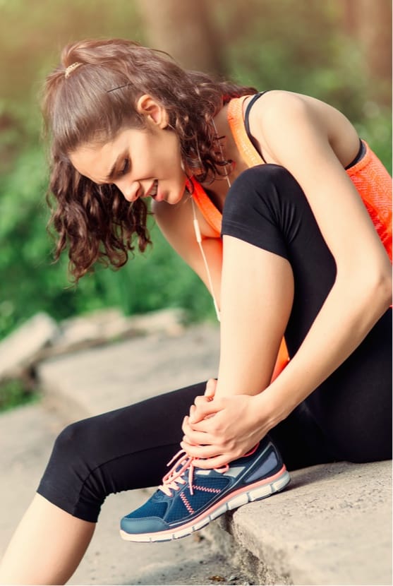 Woman sitting on stairs outside with hands on ankle in pain