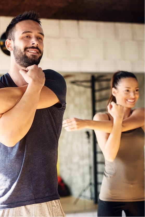 Man and woman stretching their arms across their chests at a gym
