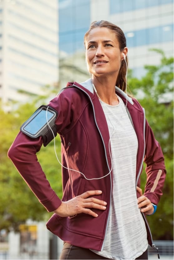 Woman standing outside wearing workout clothes and headphones in