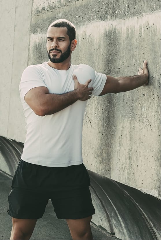 Man stretching shoulder outside using a wall for assistance